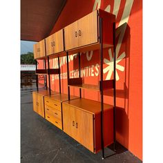 an orange wall with several wooden shelves and drawers on each shelf in front of it