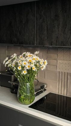 a vase filled with white daisies sitting on top of a counter next to a stove