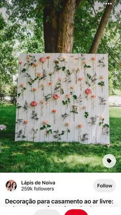 an art piece with flowers on it in front of a tree and some grass, next to a bench