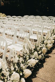 rows of white folding chairs with flowers lining the aisle for an outdoor ceremony or wedding