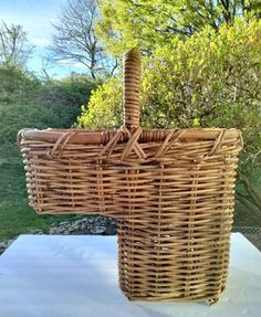 a large wicker basket sitting on top of a white cloth covered tablecloth in front of some trees