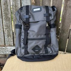 a gray and black backpack sitting on top of a wooden table next to a fence