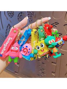 a hand holding several different key chains with cartoon characters attached to them, all in various colors and shapes