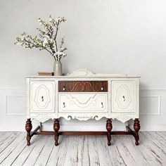 a white dresser with drawers and flowers on top of it in front of a wall