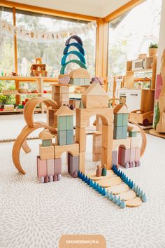 a wooden toy house sitting on top of a floor next to a pile of toys