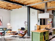 an open living room and kitchen area with exposed wood ceilinging, green cabinets, and white walls