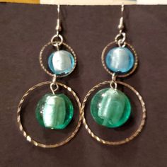 two green and blue glass beads are hanging from silver hoop earrings on a brown surface