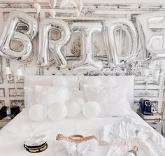 a bed with white sheets, pillows and balloons in front of a wall that says bridal