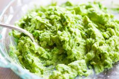 a bowl filled with green guacamole on top of a wooden table next to a spoon