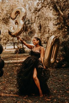 a woman in a black dress is holding balloons and posing for the camera with her number 3 balloon