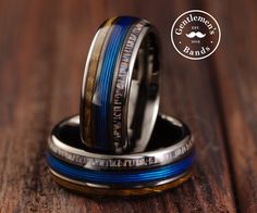 two men's wedding bands with blue and gold inlays are on top of each other