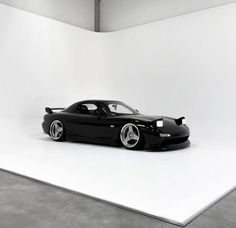 a black sports car sitting on top of a white floor in front of a wall