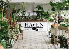 a room filled with lots of potted plants and greenery next to a sign that says haven garden cafe