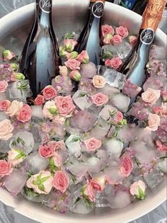 four bottles of champagne in ice with pink flowers on the rim and roses around them