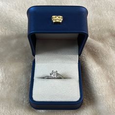 an engagement ring in a blue box on a white cloth covered surface with a gold lion head