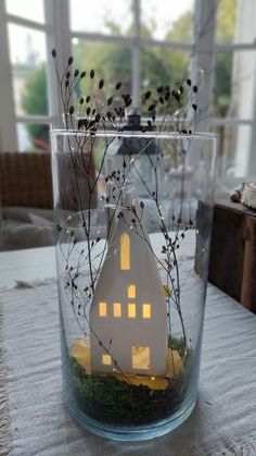 a small house in a glass vase on a table with flowers and greenery inside