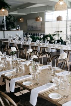 the tables are set with white flowers in vases and empty glasses on them for dinner