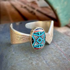 This vintage bracelet features a stamped sterling silver shank that is contemporary in style with a zig-zag-ish form atop which sits an oval bezel with intricate inlay pattern. The piece was made by Roderick and Marilyn Tenorio for Carolyn Pollack's Relios, an Albuquerque based company that employed Native American artists. From a gallery representing Tenorios: "Roderick Tenorio and his wife, Marilyn, often collaborate on making jewelry and each also works separately.  Roderick graduated from Albuquerque High School in 1981, then attended the Institute of American Indian Arts in Santa Fe. He served time in the U. S. Army. He is a top prizewinning artist from Santo Domingo Pueblo. Marilyn Tenorio is a Navajo and works in mosaic inlay as well as silver and gold jewelry." Examine the oval-sha Southwestern Turquoise Etched Jewelry, Southwestern Etched Turquoise Jewelry, Southwestern Style Etched Turquoise Jewelry, Engraved Turquoise Sterling Silver Bracelet Gift, Artisan Turquoise Engraved Bracelets, Artisan Turquoise Engraved Bracelet, Adjustable Stamped Turquoise Bracelets, Adjustable Turquoise Stamped Bracelets, Southwestern Engraved Cuff Bracelet As A Gift