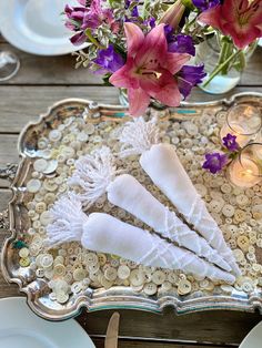 two white napkins are on a silver tray with flowers in the vase behind it