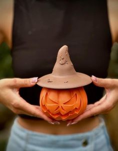 a woman holding an orange pumpkin in her hands with a witch hat on it's head