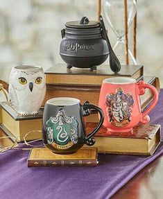 three harry potter mugs are sitting on top of books and an owl figurine is next to them