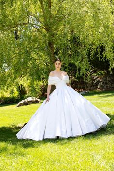 a woman in a white wedding dress is standing under a tree and posing for the camera