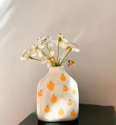 a white vase filled with flowers on top of a green table next to a wall