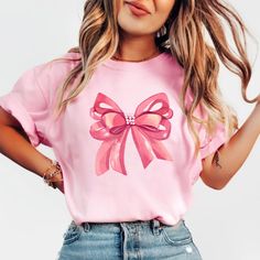 Embrace elegance and flirtatious charm with our captivating pink bow shirt, a delightful addition to your coquette-inspired wardrobe! 🌸👚 This shirt embodies the essence of femininity and playfulness, perfect for those who adore a touch of chic sophistication with a hint of flirtation. 🌷 The darling pink hue complements the shirt's design, accentuating the focal point--an exquisitely crafted oversized bow adorning the neckline or sleeves, adding a whimsical and flirtatious allure to your ensem Cute Bow T-shirt For Spring, Cute Pink T-shirt With Bow, Feminine Pink Summer Shirt, Feminine Pink Shirt For Summer, Feminine Pink Crew Neck T-shirt, Casual Party Tops With Bow, Spring Party Tops With Ribbon, Feminine Tops With Ribbon For Spring, Feminine Ribbon Tops For Spring