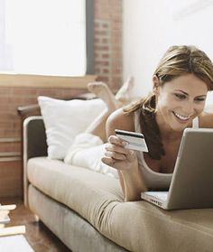 a woman laying on a couch holding a credit card and looking at her laptop