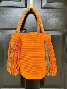 an orange handbag hanging on a door with beaded handles and tassels