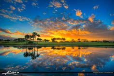 the sun sets over a lake with palm trees in the foreground and clouds in the background