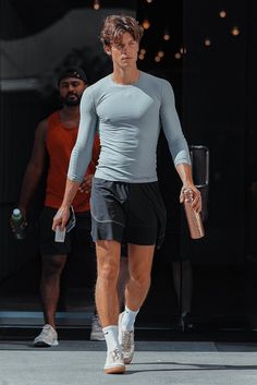 a man in grey shirt and black shorts walking down the street with his hand on his hip