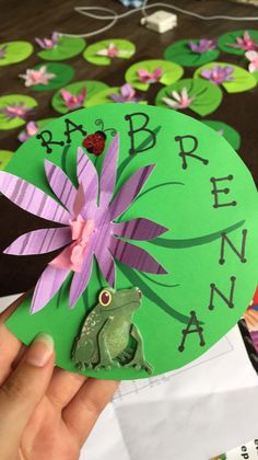 a person holding up a paper frog with flowers on it's head and name