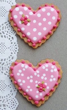 two decorated heart shaped cookies sitting on top of a lace doily next to each other