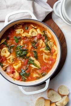 a pot filled with pasta and spinach on top of a wooden cutting board next to crackers