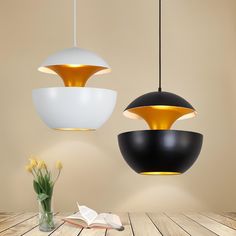 two black and white pendant lights hanging over a wooden table with a book on it