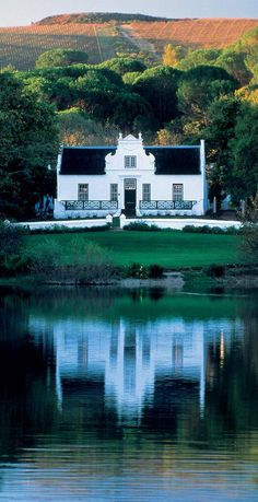 a large white house sitting on top of a lush green hillside next to a lake