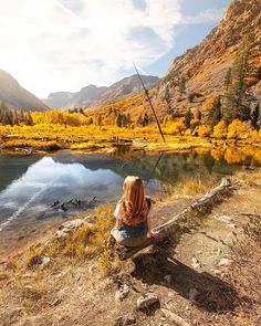 a woman sitting on a log next to a lake