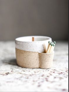 two matchsticks in a ceramic cup on a countertop with speckled surface