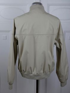 "This classic collegiate-look ivory beige jacket has a soft acrylic knit collar and ribbed cuffs and waistband. The lightweight jacket zips closed in front and closes further with two buttons on the waistband and another at the neckline. The jacket has three stainless steel airing grommets at the back of each underarm seam. Brand label: Hill & Archer (Made in China) Size: 42 to 44 US/UK Material: 65% polyester, 35% cotton Chest = 46 inches (116.84cm) (This is a Size 44 US/UK; the extra space Casual Beige Outerwear With Ribbed Collar, Beige Casual Outerwear With Ribbed Collar, Cream Outerwear With Ribbed Cuffs For Work, Fitted Beige Outerwear With Ribbed Cuffs, Solid Collared Outerwear With Ribbed Cuffs, Cream Outerwear With Ribbed Collar For Fall, Classic Beige Outerwear With Ribbed Cuffs, Long Overcoat, Beige Jacket