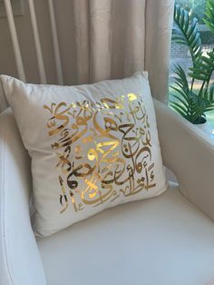 a white chair in front of a window with a gold foiled pillow on it