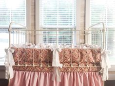 a crib with pink and white bedding in front of two windows