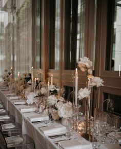 a long table is set with white flowers and candles for an elegant dinner or reception