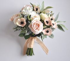 a bouquet of white and pink flowers is tied to a gray wall with a brown ribbon