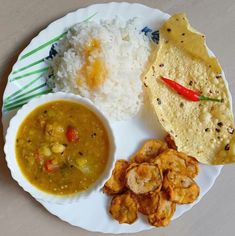 a white plate topped with rice and soup next to fried food on top of it