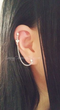 a woman with long black hair wearing a silver chain ear cuff