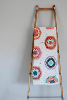 a crocheted blanket is hanging on a wooden ladder in front of a gray wall