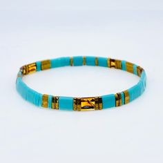 a turquoise and gold beaded bracelet on a white background