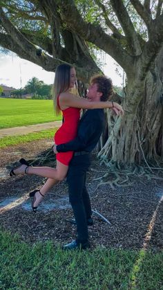 a man and woman dancing in front of a large tree with their arms around each other