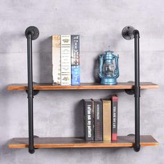 two wooden shelves with books on them against a gray wall, one shelf has an iron pipe and the other is wood